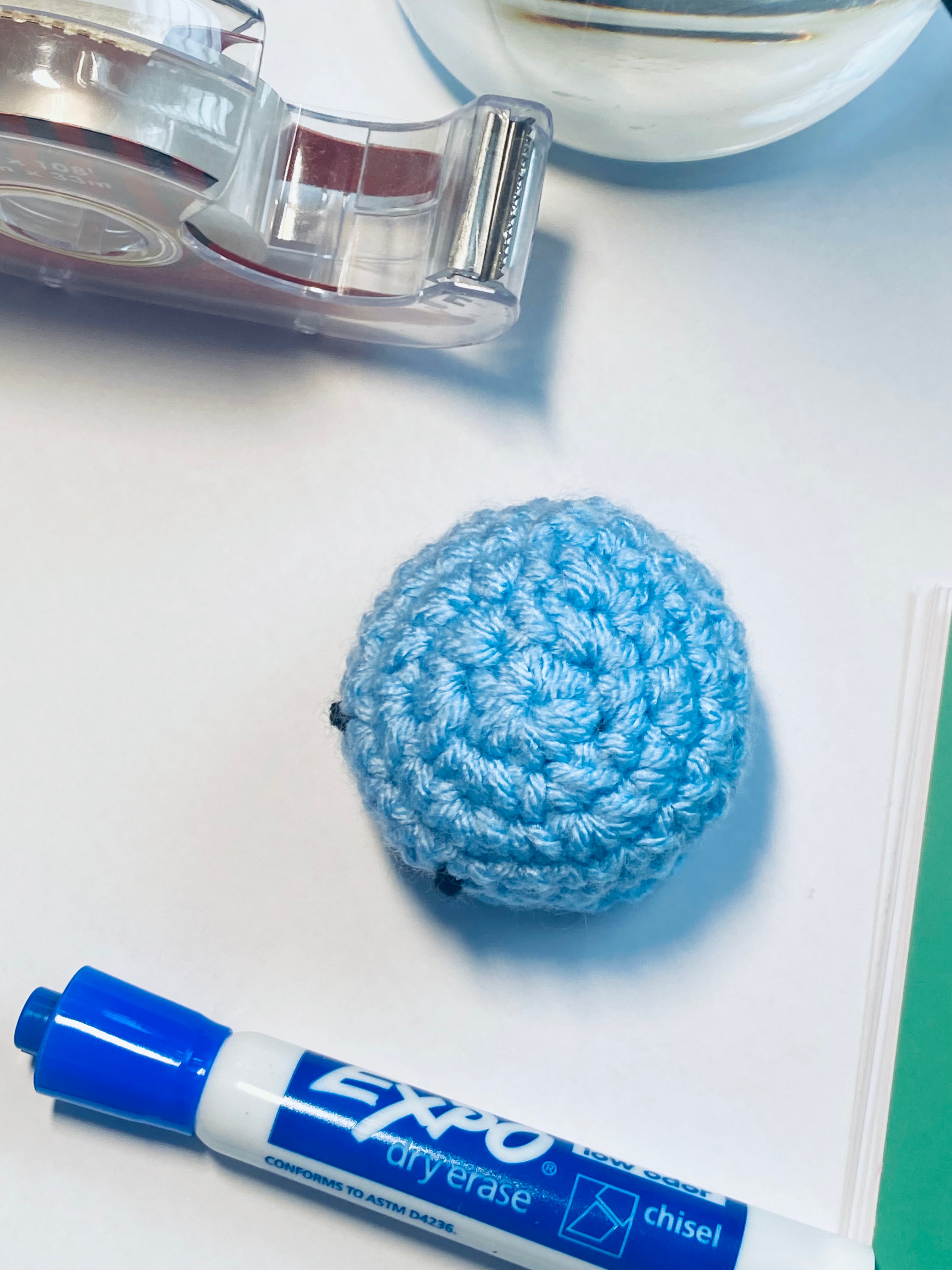 Blue crocheted ball and Expo dry erase marker on a white surface