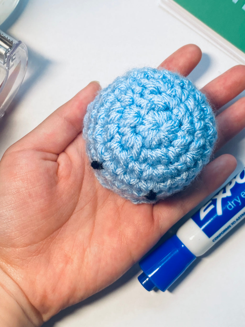 Blue crocheted ball held in a hand with a blue marker in the background